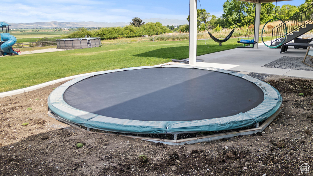 View of green lawn with a trampoline, a mountain view, and an outdoor pool