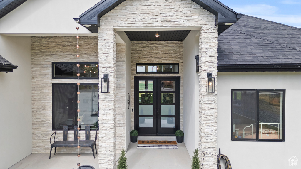 Doorway to property featuring stucco siding, stone siding, a shingled roof, and covered porch