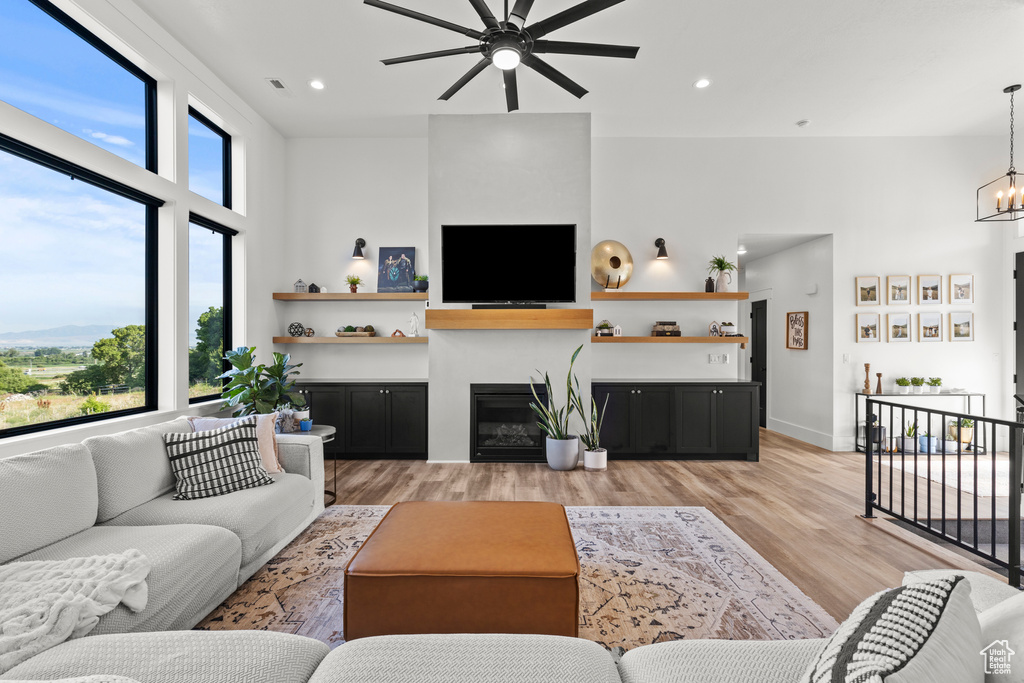 Living area featuring a ceiling fan, light wood-type flooring, recessed lighting, a chandelier, and a glass covered fireplace