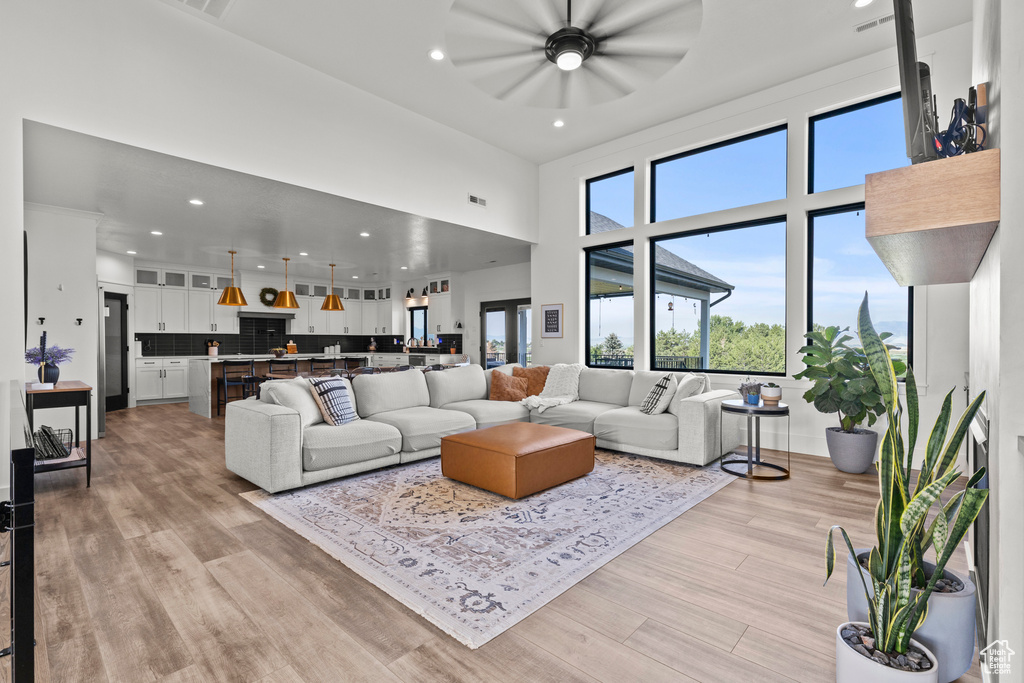 Living room with ceiling fan, plenty of natural light, light wood-style flooring, a towering ceiling, and recessed lighting