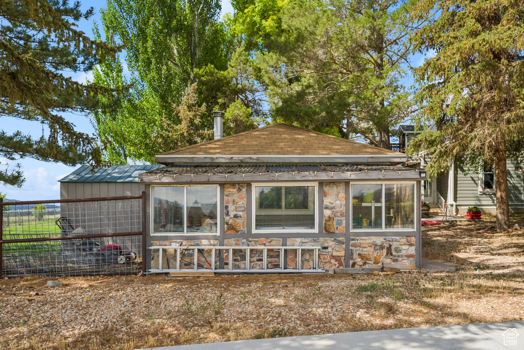Back of property featuring stone siding, exterior structure, board and batten siding, an outdoor structure, and a shingled roof