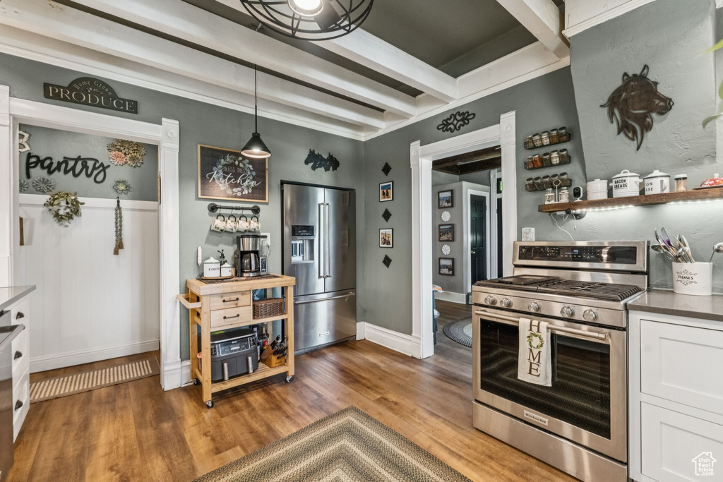 Kitchen with stainless steel appliances, wood finished floors, beamed ceiling, white cabinetry, and hanging light fixtures
