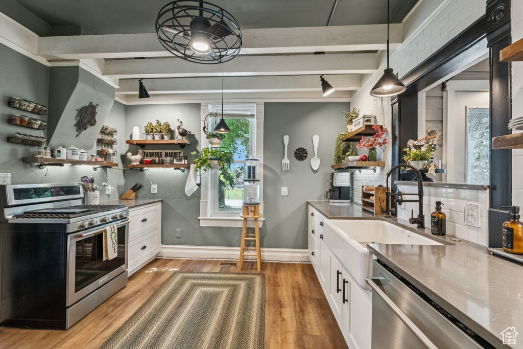 Kitchen with appliances with stainless steel finishes, light wood finished floors, white cabinetry, open shelves, and hanging light fixtures