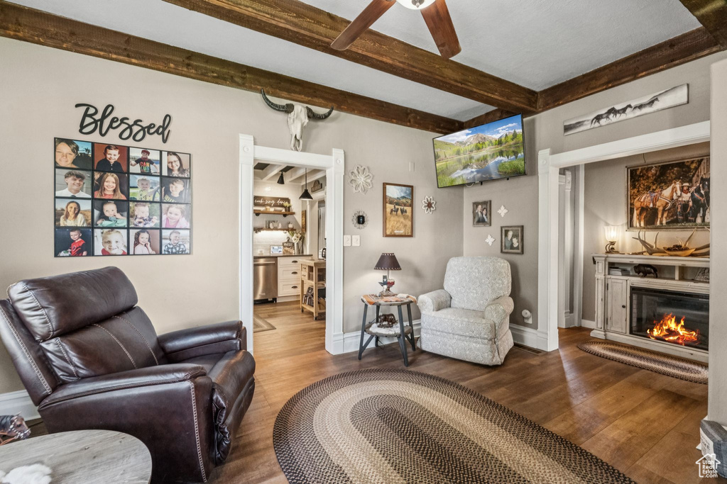Living area with wood finished floors, beamed ceiling, a glass covered fireplace, and ceiling fan