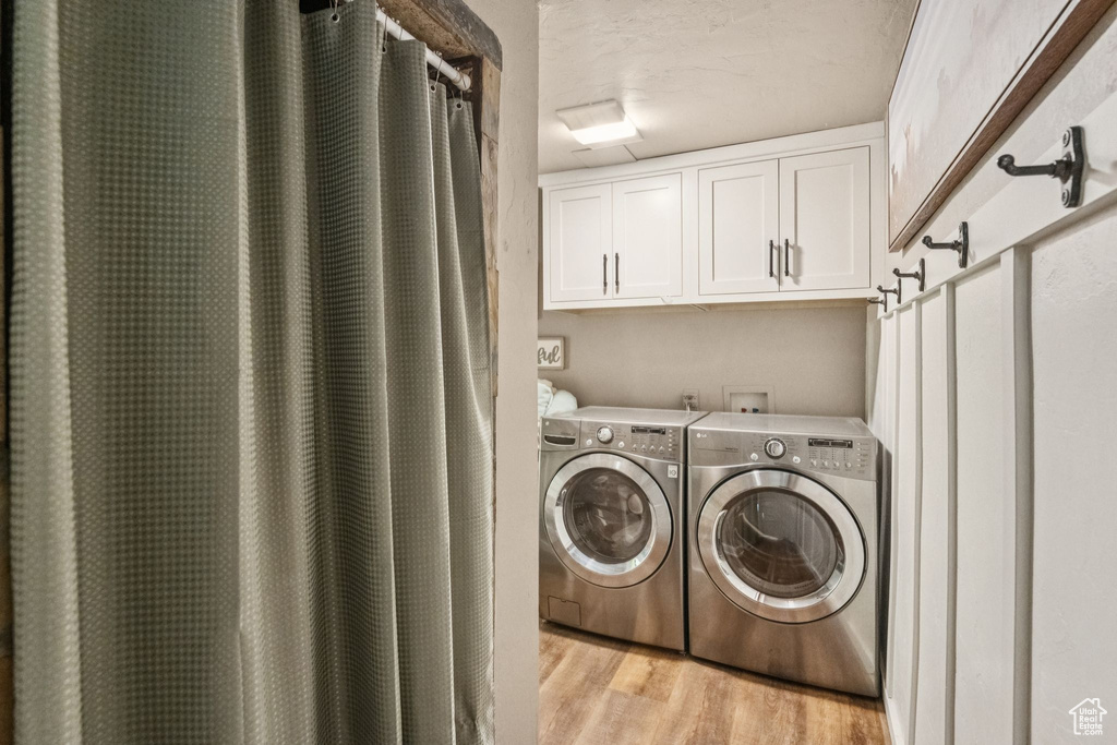 Washroom with washing machine and clothes dryer, light wood-style flooring, and cabinet space