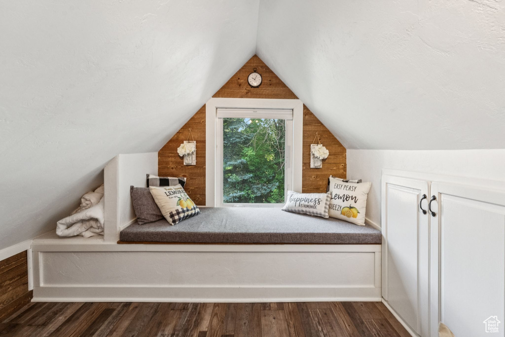 Unfurnished bedroom with lofted ceiling, wood walls, and dark wood finished floors