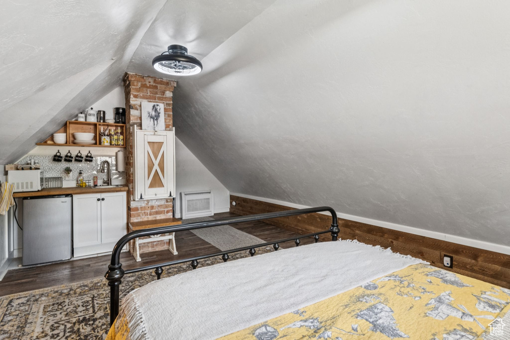 Bedroom with wood finished floors, lofted ceiling, freestanding refrigerator, and bar area