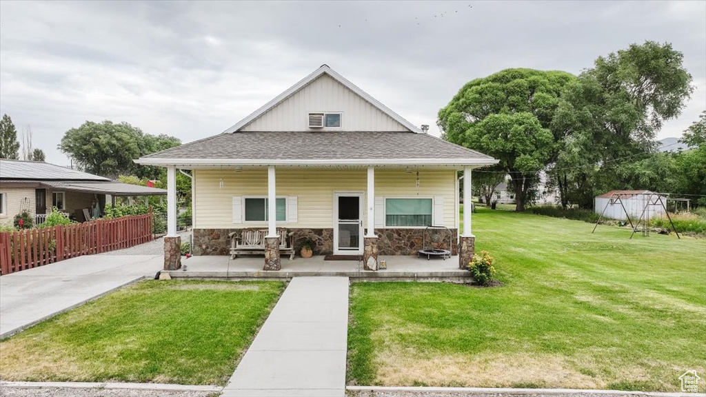View of front of property featuring covered porch, a front yard, stone siding, a storage unit, and roof with shingles