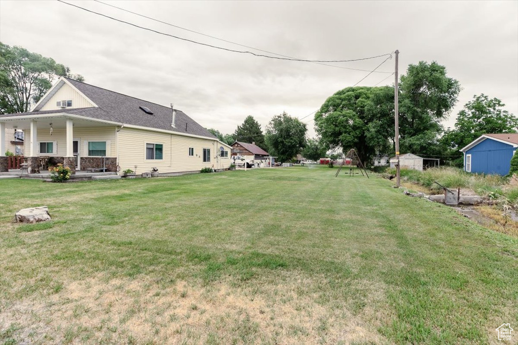 View of grassy yard featuring a porch and a storage unit
