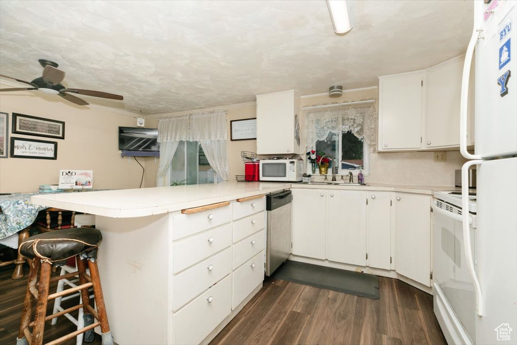 Kitchen featuring white appliances, a peninsula, a ceiling fan, dark wood-style flooring, and light countertops