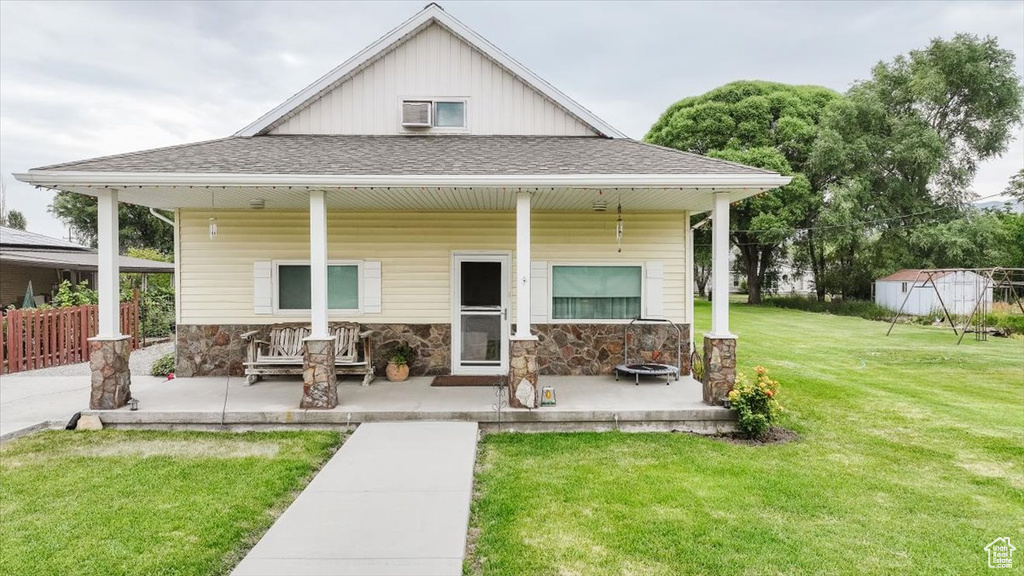 View of front of home with a porch, a front lawn, a shingled roof, and stone siding