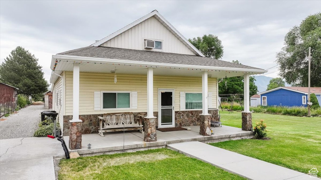 View of front of home featuring a front yard, stone siding, board and batten siding, covered porch, and a shingled roof