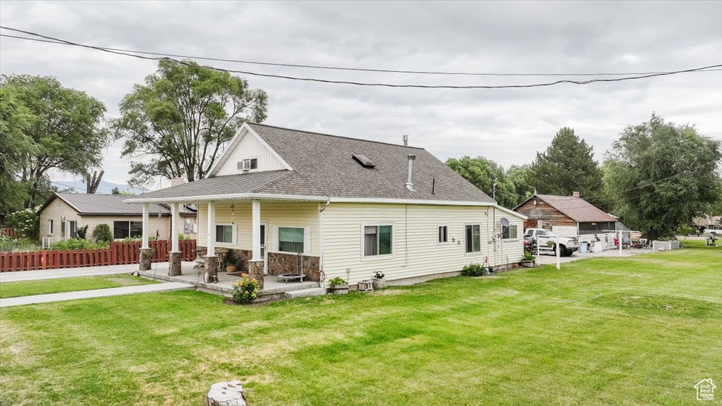 Back of property with a yard, a shingled roof, stone siding, and covered porch