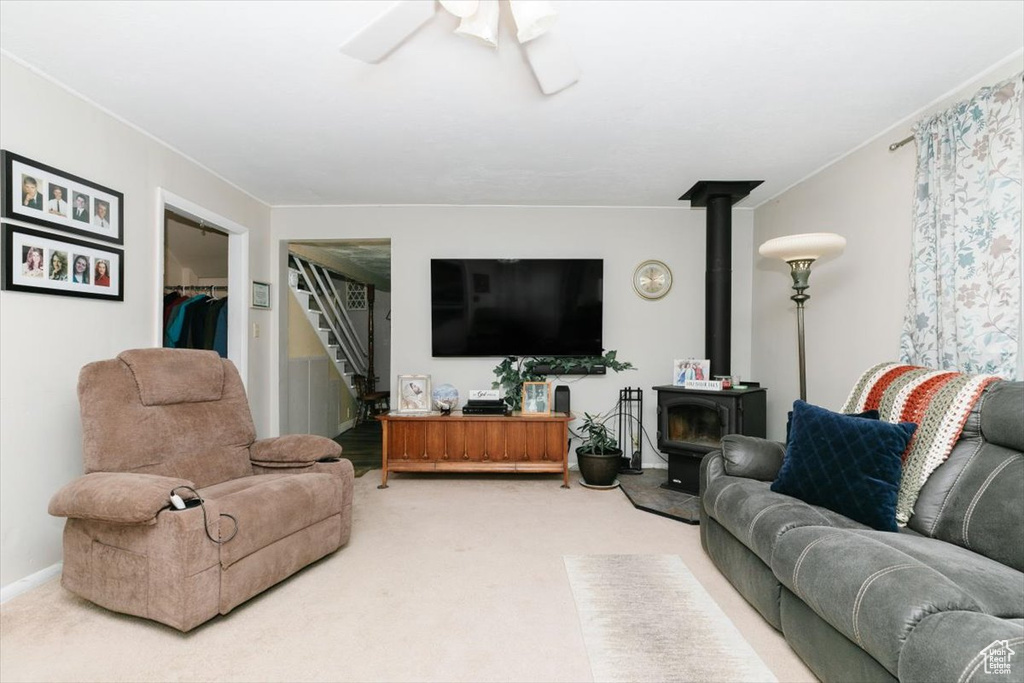 Carpeted living area featuring a wood stove, stairway, and ceiling fan