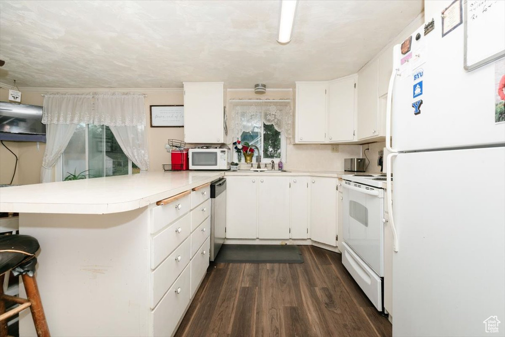 Kitchen featuring white appliances, a peninsula, light countertops, dark wood-style flooring, and white cabinetry