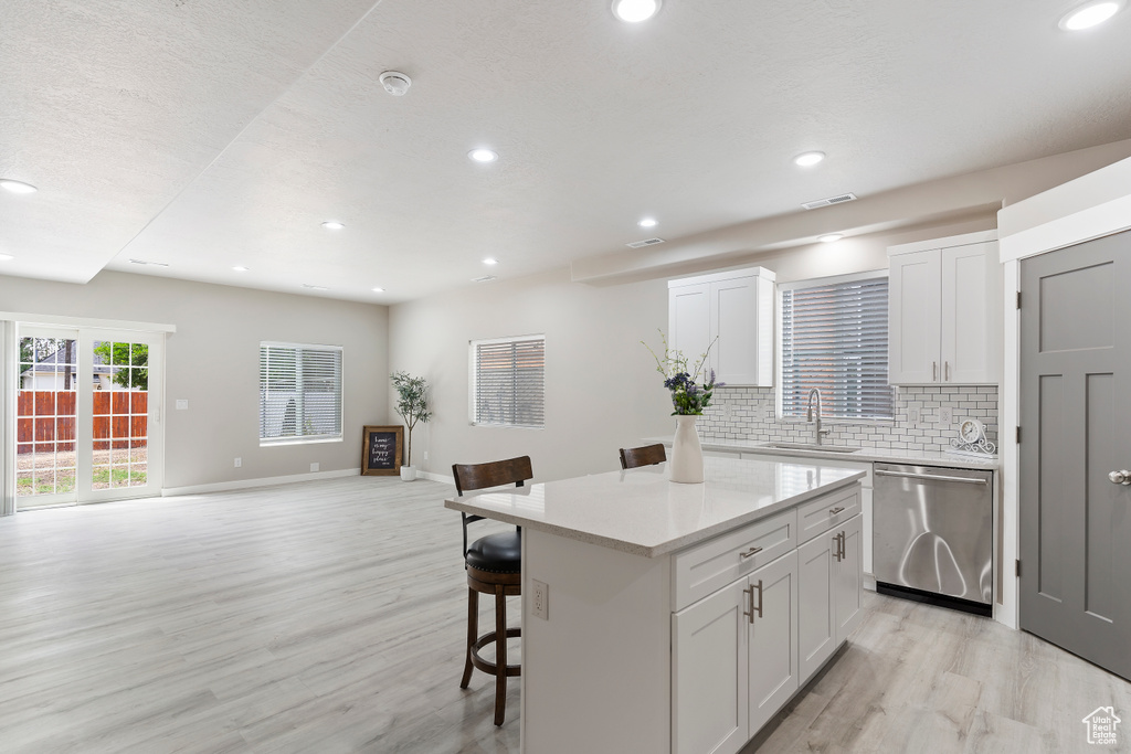 Kitchen with dishwasher, light wood-type flooring, a kitchen bar, a kitchen island, and backsplash