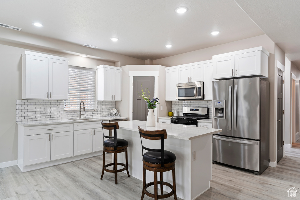 Kitchen with appliances with stainless steel finishes, a kitchen breakfast bar, light wood-type flooring, white cabinets, and a center island
