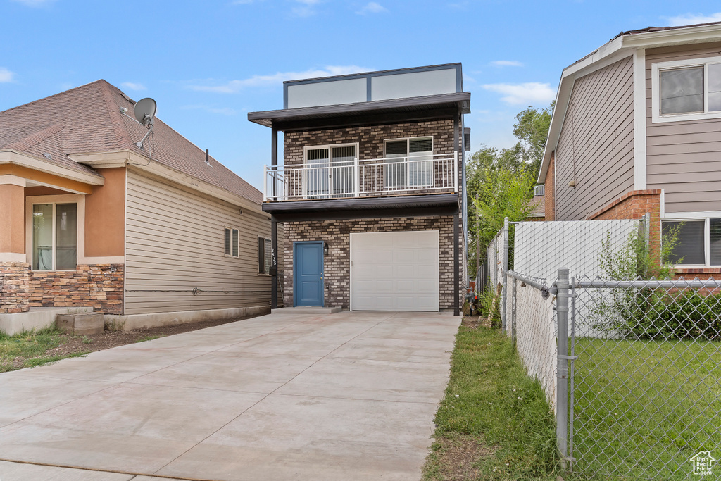 View of front of home with a balcony, concrete driveway, a garage, and brick siding