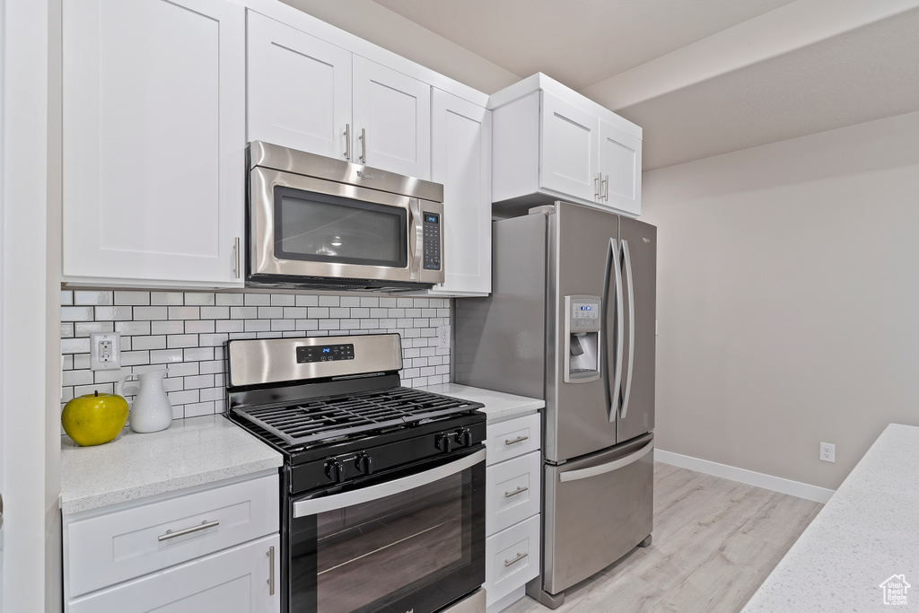 Kitchen with appliances with stainless steel finishes, light wood-type flooring, tasteful backsplash, and white cabinets