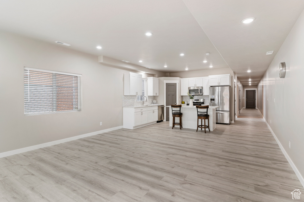 Kitchen featuring appliances with stainless steel finishes, a kitchen bar, tasteful backsplash, white cabinets, and light wood-type flooring