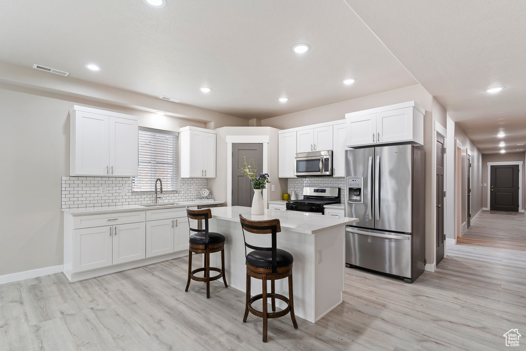 Kitchen with stainless steel appliances, a breakfast bar, light wood finished floors, a kitchen island, and recessed lighting