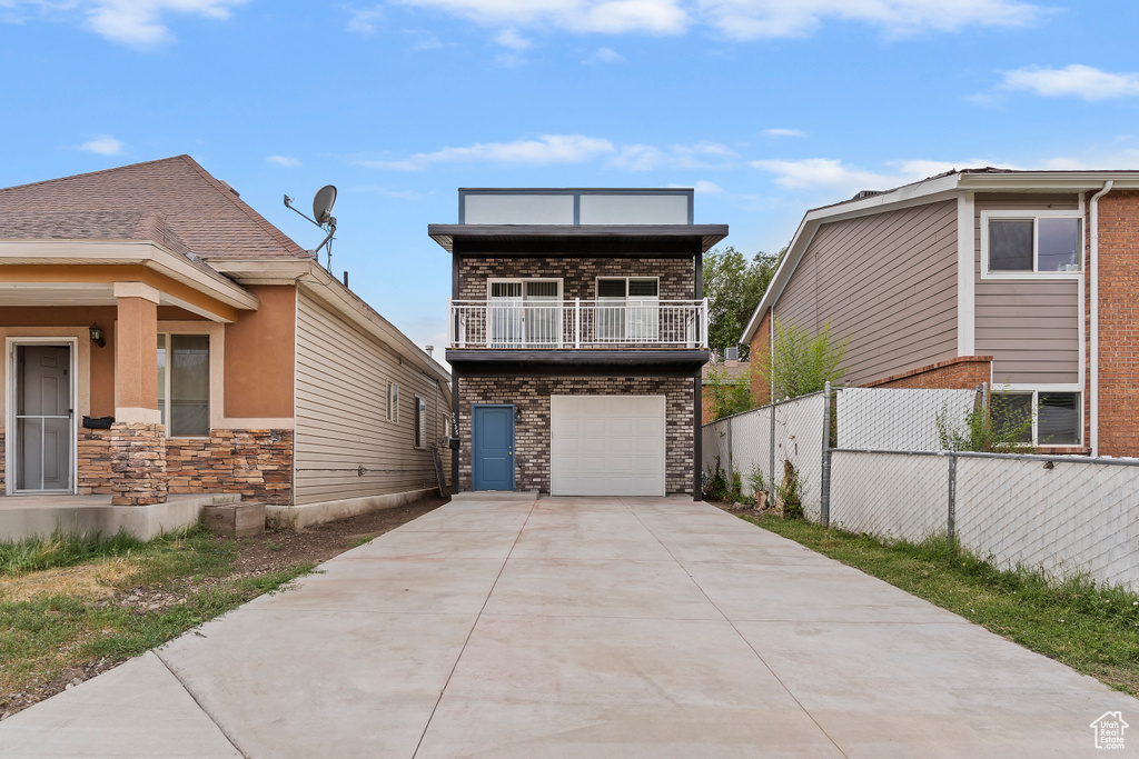 View of front of home with concrete driveway, a balcony, a garage, and brick siding