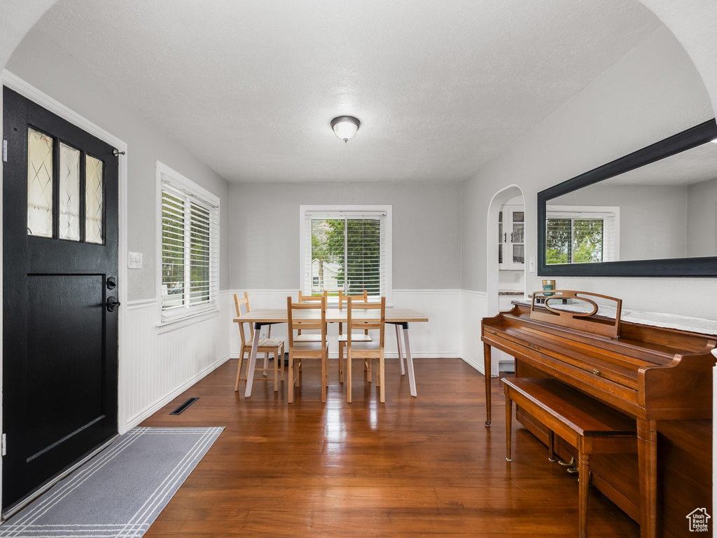 Dining space with arched walkways, a wainscoted wall, and wood finished floors