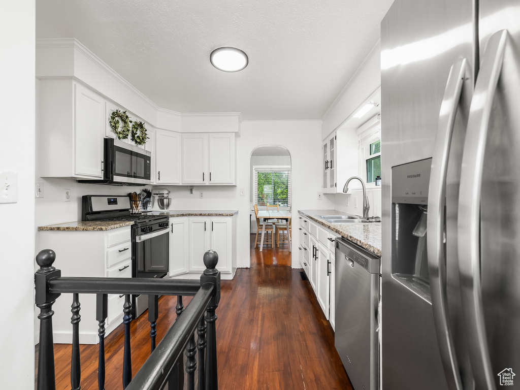 Kitchen with appliances with stainless steel finishes, arched walkways, light stone countertops, and white cabinets