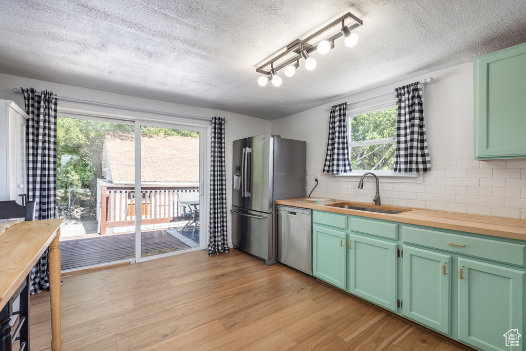 Kitchen featuring stainless steel appliances, wood counters, decorative backsplash, a textured ceiling, and light wood-style floors