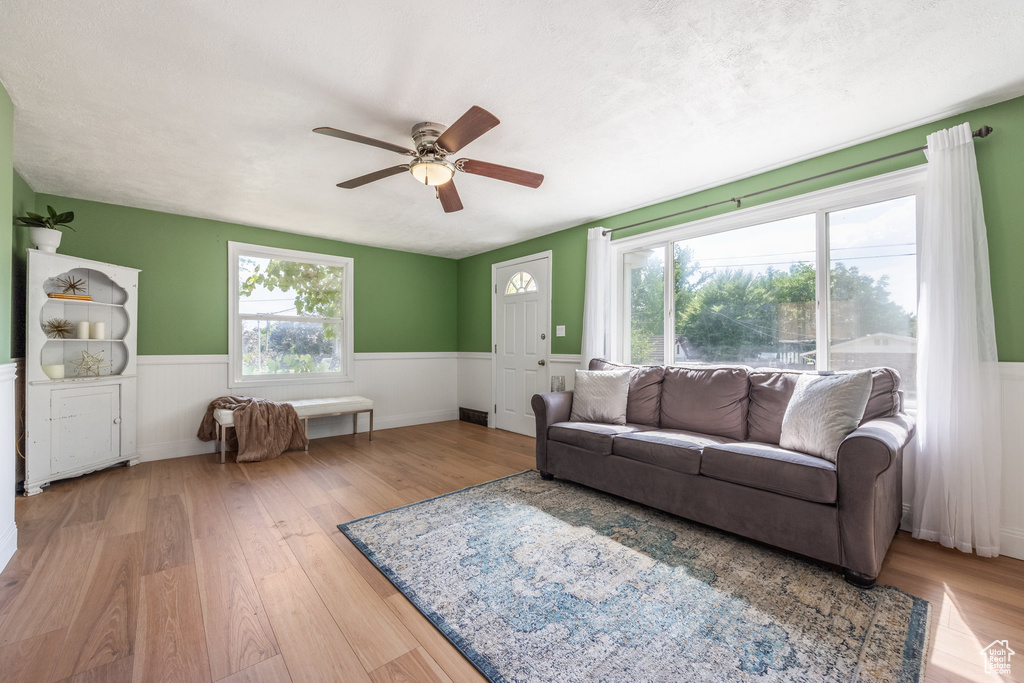 Living area featuring a wainscoted wall, ceiling fan, wood finished floors, and plenty of natural light