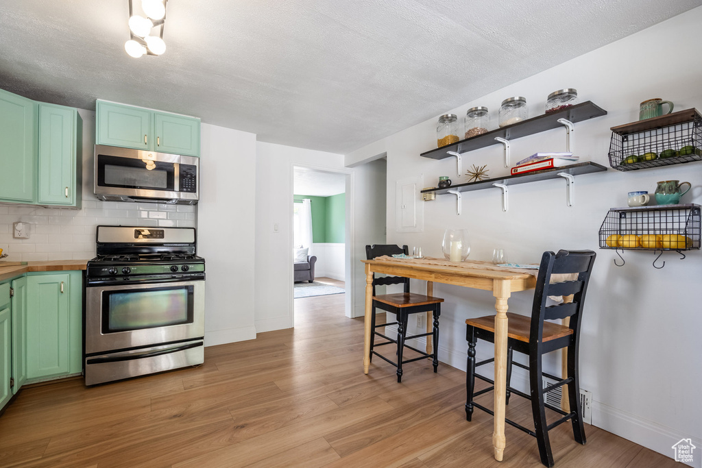Kitchen with appliances with stainless steel finishes, light wood-style flooring, tasteful backsplash, and green cabinets