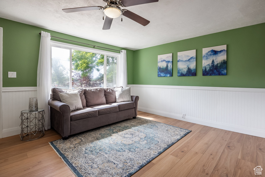 Living room with a wainscoted wall, wood finished floors, and a ceiling fan