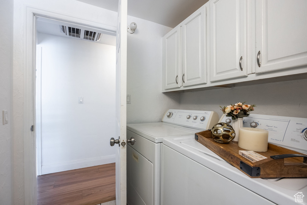 Laundry area featuring washing machine and dryer, cabinet space, and wood finished floors