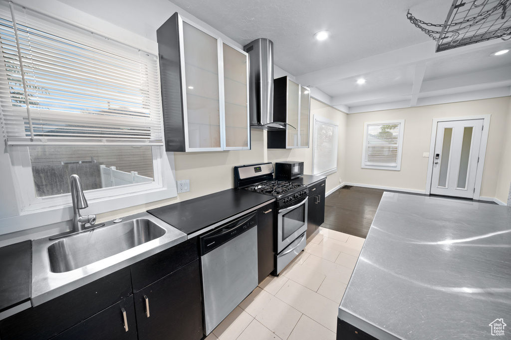 Kitchen featuring appliances with stainless steel finishes, stainless steel counters, dark cabinets, recessed lighting, and wall chimney exhaust hood
