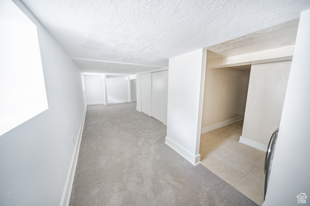 Hall with a textured ceiling, light tile patterned floors, and light carpet