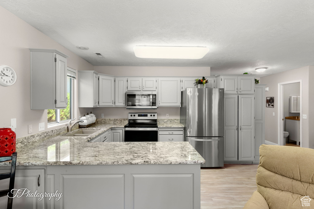 Kitchen with stainless steel appliances, a peninsula, light wood-type flooring, light stone counters, and a textured ceiling