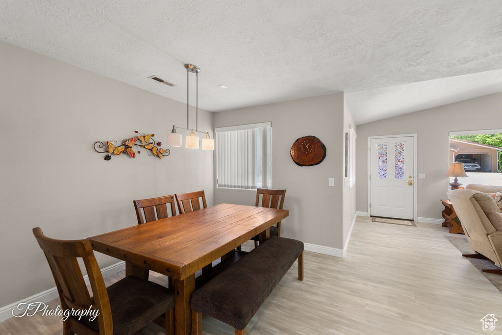 Dining area with light wood-style flooring, a textured ceiling, and vaulted ceiling