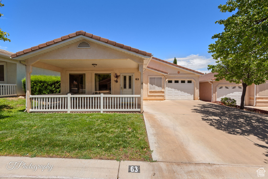 View of front of home with an attached garage, concrete driveway, a front yard, a porch, and a tiled roof