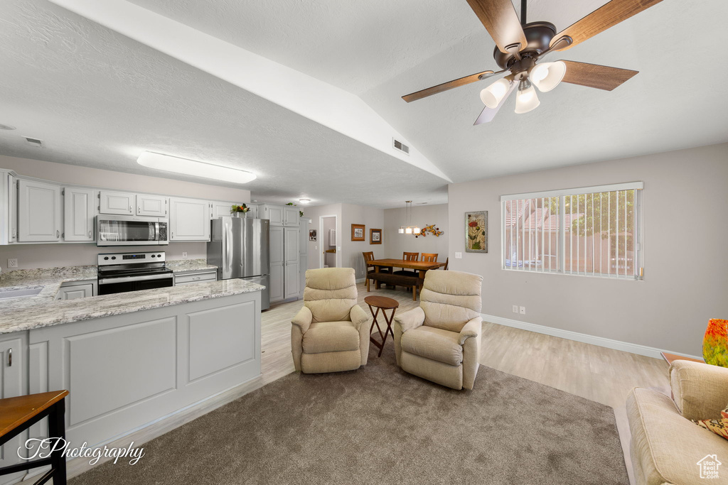 Living area with light wood-style floors, vaulted ceiling, and a ceiling fan