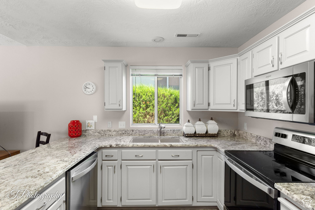 Kitchen with stainless steel appliances, white cabinets, a textured ceiling, and light stone counters