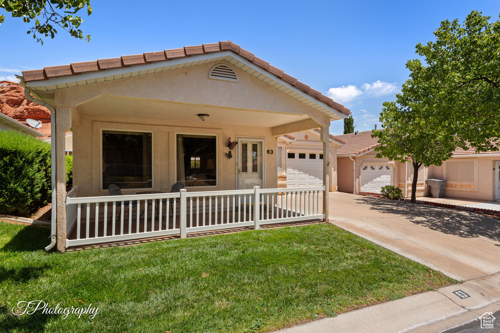 View of front of home with an attached garage, concrete driveway, a front lawn, and a tiled roof