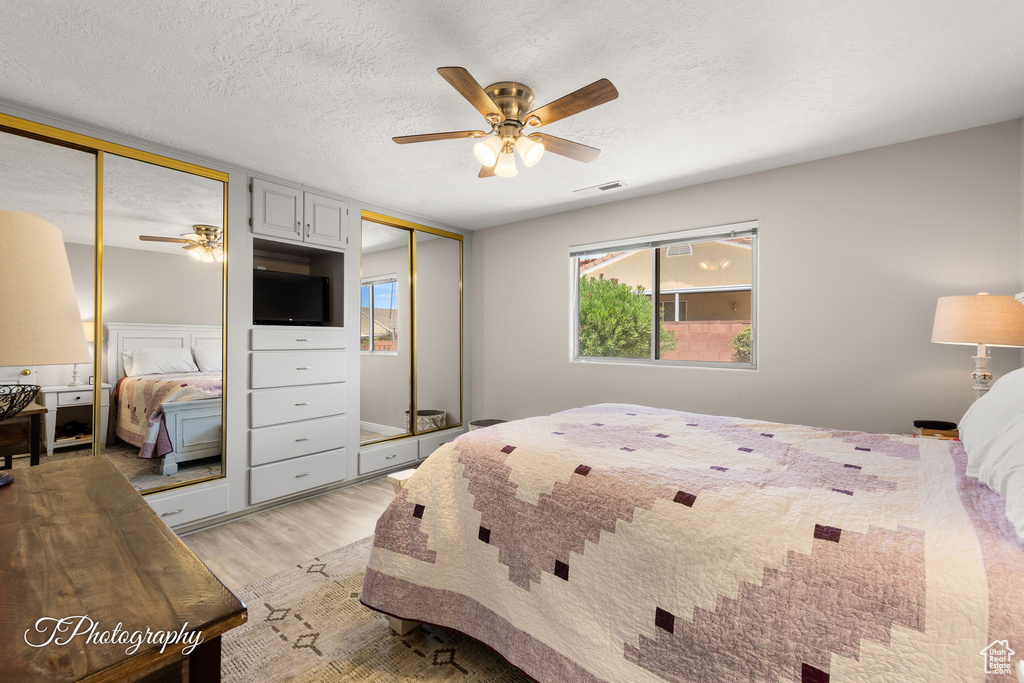 Bedroom featuring multiple closets, light wood-type flooring, a textured ceiling, and ceiling fan