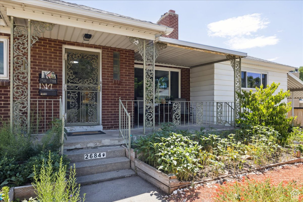 Property entrance featuring covered porch, a chimney, and brick siding