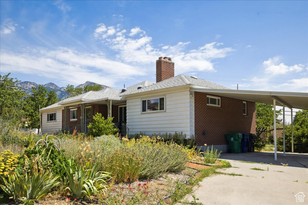Rear view of house with an attached carport, asphalt driveway, brick siding, a chimney, and a mountain view