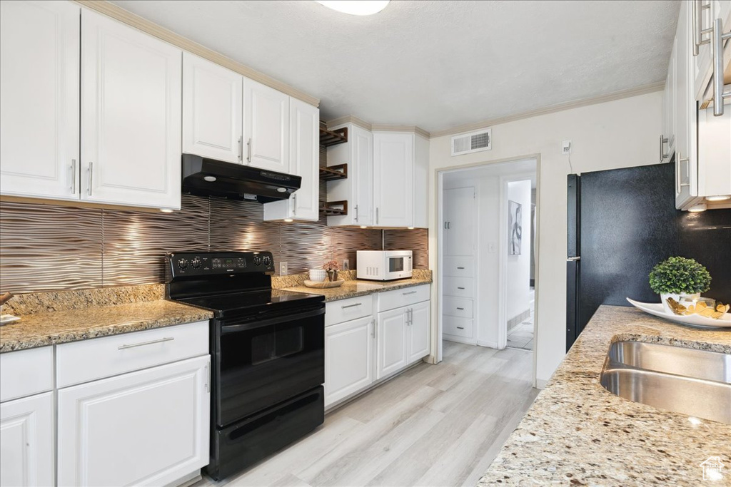 Kitchen featuring black range with electric cooktop, under cabinet range hood, white microwave, white cabinets, and crown molding