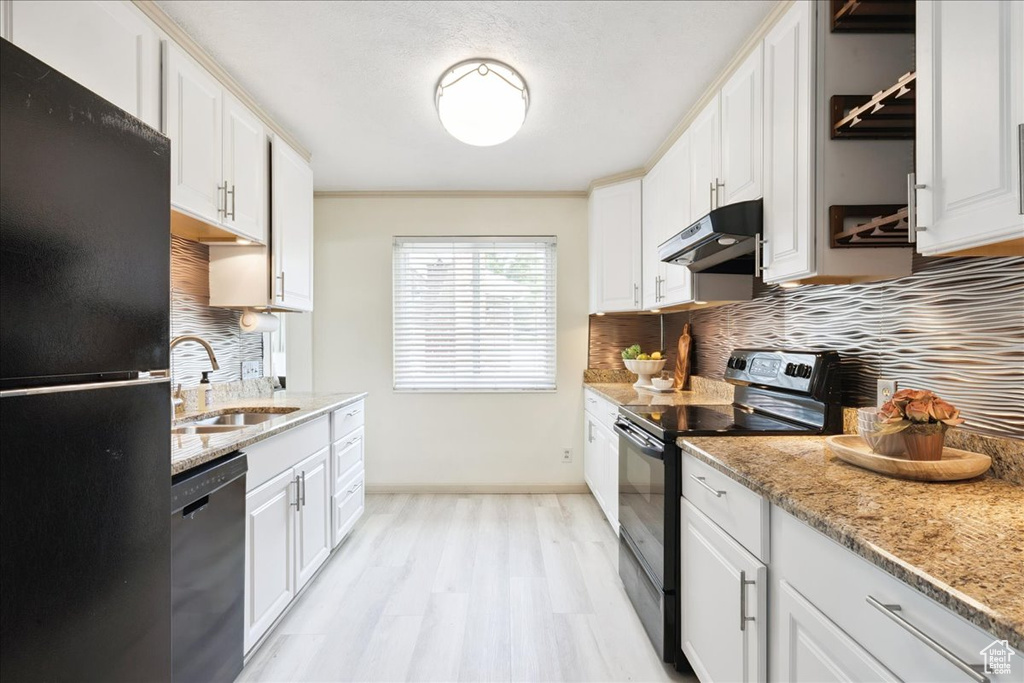 Kitchen featuring black appliances, under cabinet range hood, decorative backsplash, light wood-style floors, and white cabinets