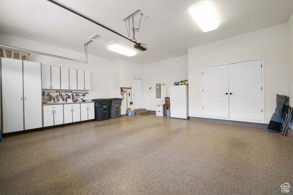 Garage featuring freestanding refrigerator, electric panel, and a garage door opener