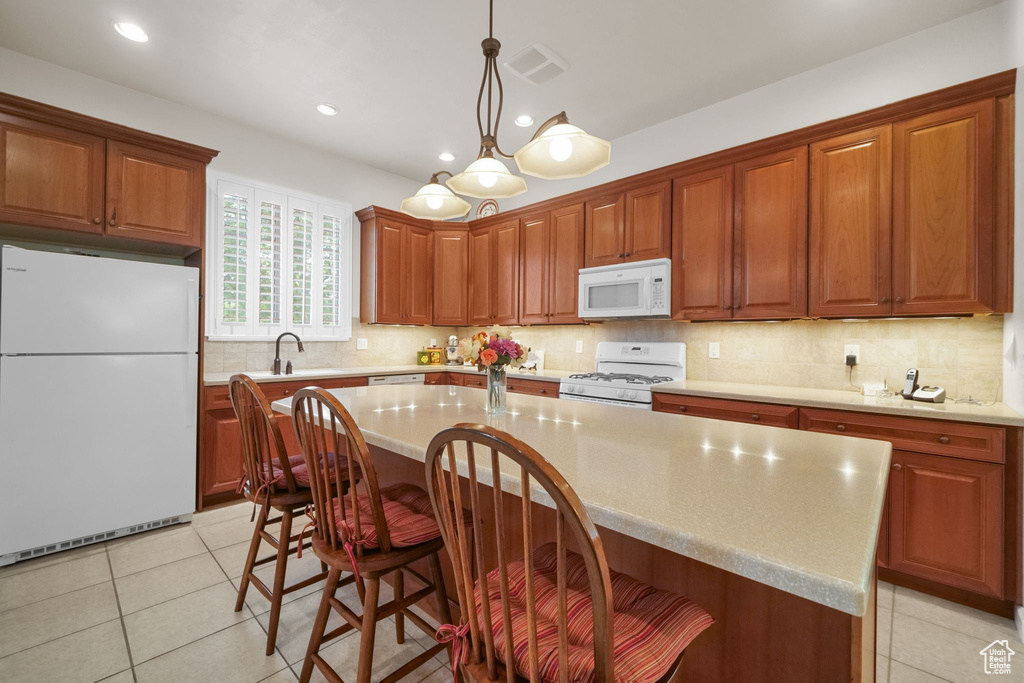 Kitchen with white appliances, light countertops, a kitchen island, backsplash, and a kitchen bar