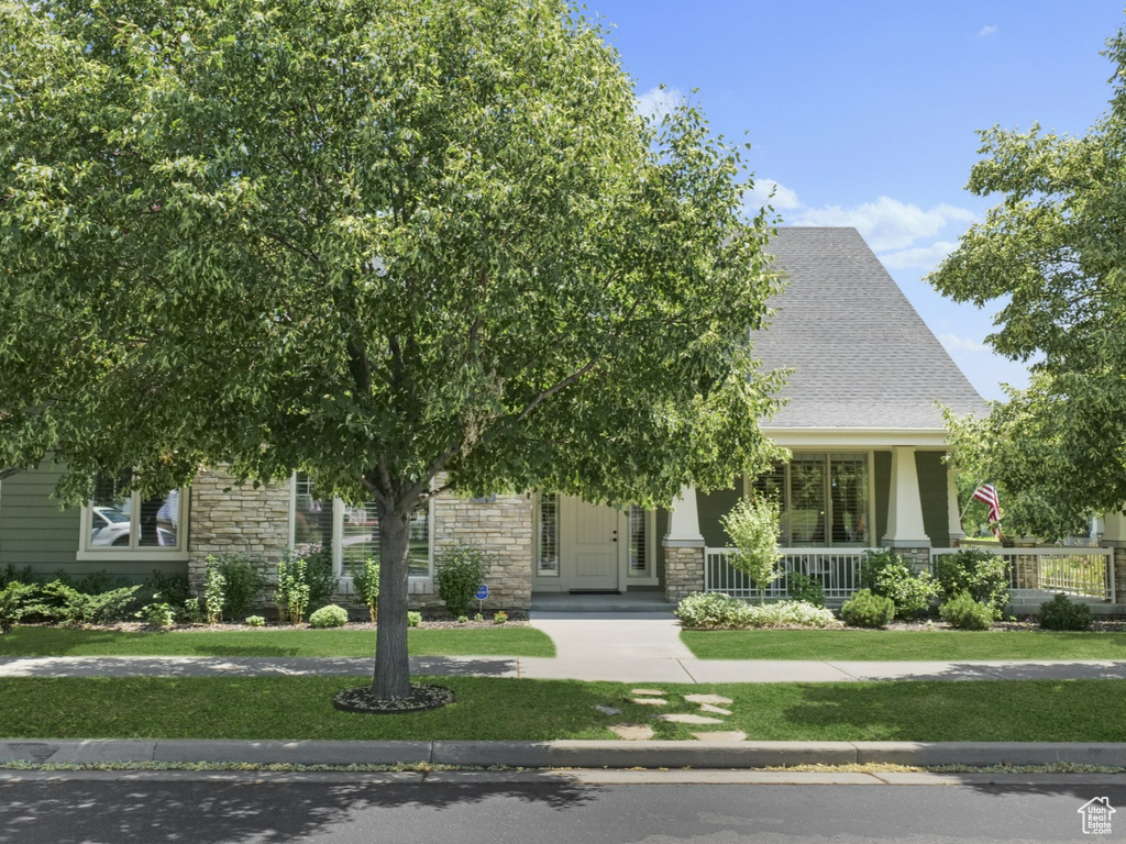 View of property hidden behind natural elements with stone siding, covered porch, and a front lawn