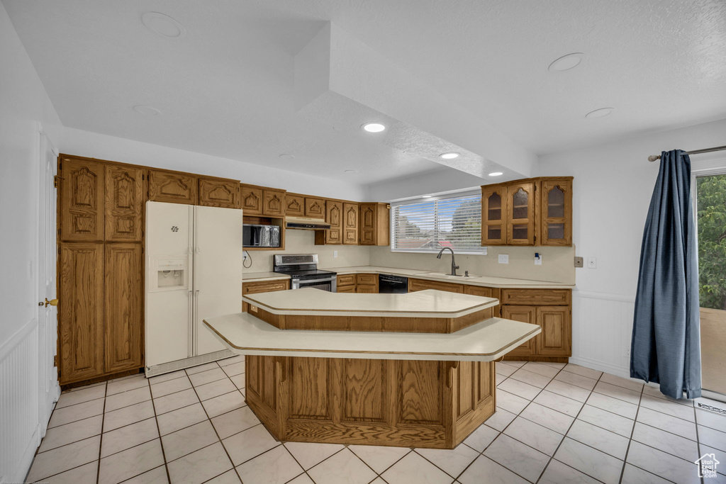 Kitchen with appliances with stainless steel finishes, brown cabinetry, light countertops, recessed lighting, and a center island